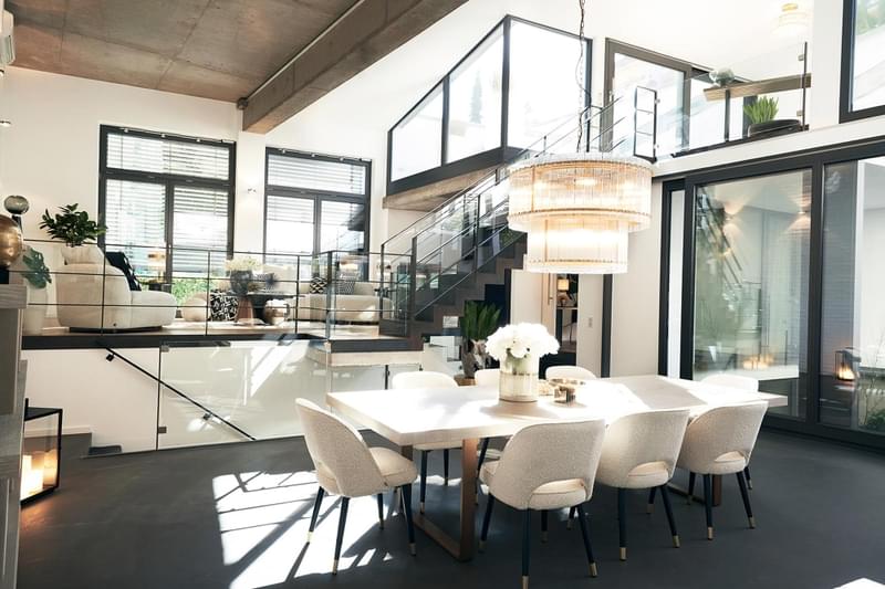 A modern loft with home interior design consisting of table, chairs, flooring, windows and interesting architecture.
